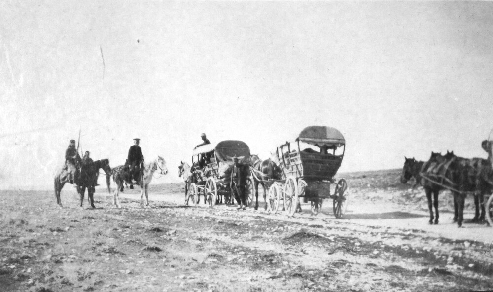 Riders halt with hooded wagons on open ground. c. 1919-1922.