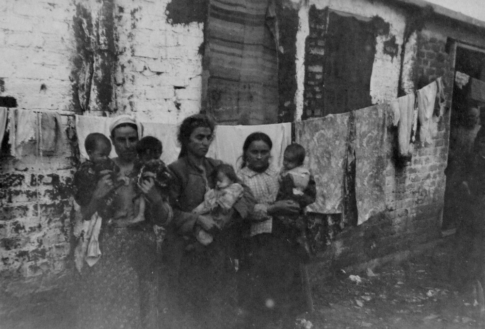 Three women hold children by a barracks wall. Camp Lembet, Salonica, 1922.