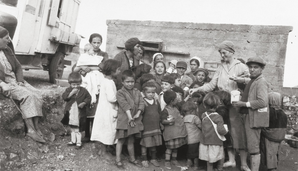 Annie Slack distributes quinine solution candy to children, with the wheels of her mobile clinic visible at left. Syria, 1930. Slack provided the only source of medical care to hundreds of resettled refugees and native inhabitants.