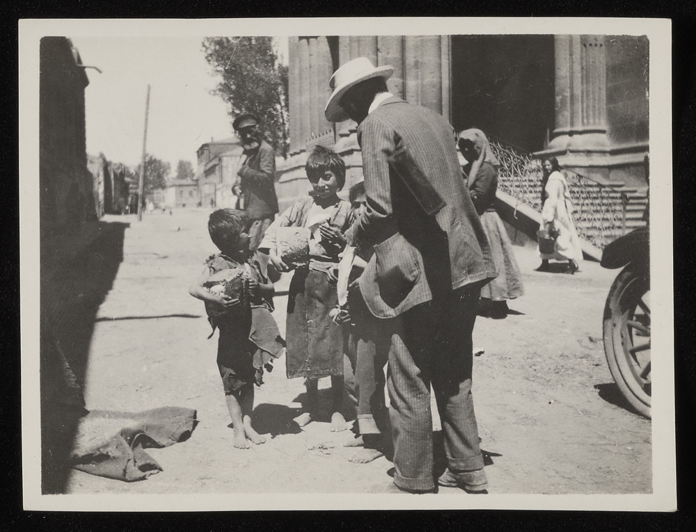 Man in white hat, possibly Jaquith, handing bread to boys, Caucasus, 1920s
