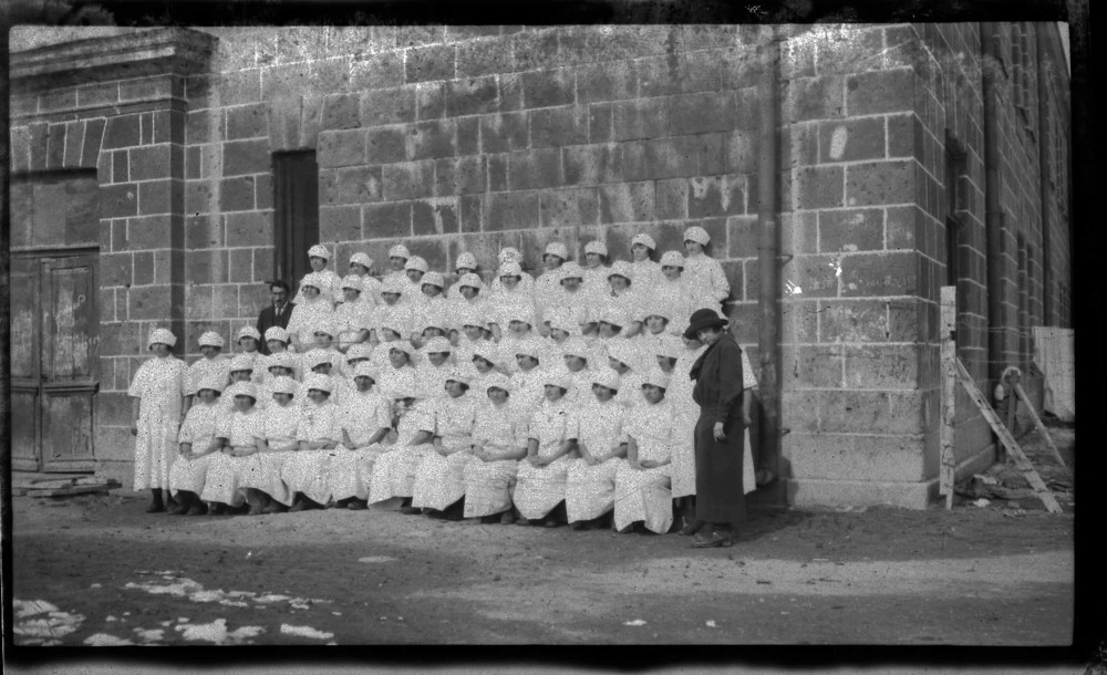 Nurses pose in rows beside a stone building.