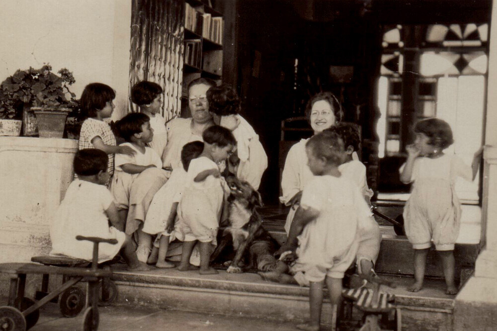 Maria Jacobsen and Nellie Miller Mann sit on the steps of the Birds' Nest orphanage with small children. Sidon, c. 1921–1923.