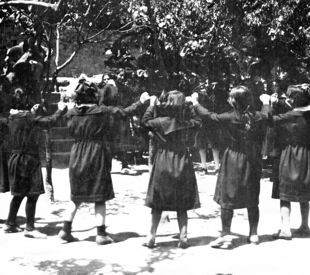 Girls join hands in an outdoor circle dance.