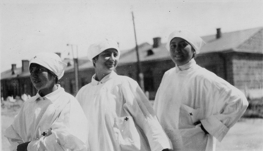 Three nurses pose outdoors in white uniforms.