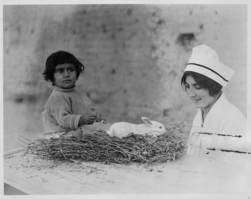 A child sits with a white rabbit as a nurse looks on.