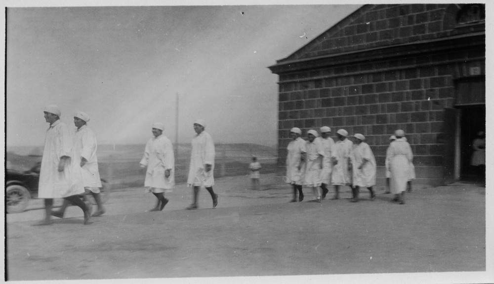Nurses walk in a line beside a stone building.