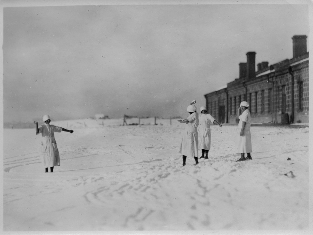 Nurses stand in the snow beside a stone building.