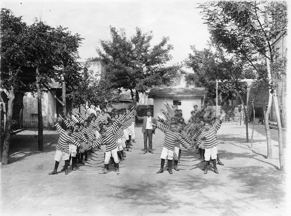 Boys perform stretching exercises in rows outdoors.
