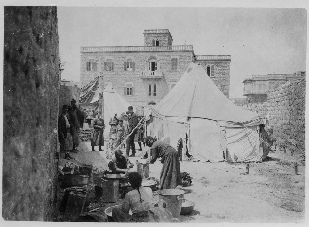 Refugees cook and wash beside a canvas tent pitched against a stone building, Beirut, c. 1921–1923 — 